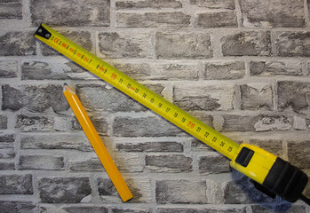 Yellow construction tape measure and yellow pencil on brick background.