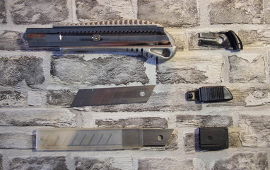Disassembled stationery knife, blade replacement in knife on a brick wall background.