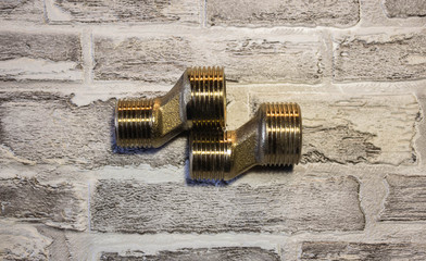 Threaded metal adapter for connecting water to the bathroom. Against the background of a brick wall.