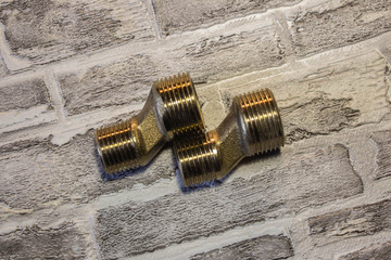 Threaded metal adapter for connecting water to the bathroom. Against the background of a brick wall.