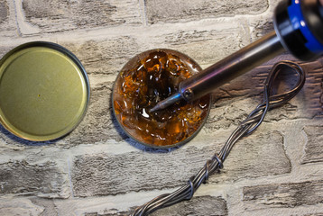 Soldering iron with a blue handle, rosin and soldering tin on a brick wall background.