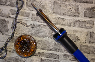 Soldering iron with a blue handle, rosin and soldering tin on a brick wall background.