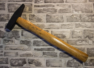 Black metal hammer with wooden handle on a brick wall background.