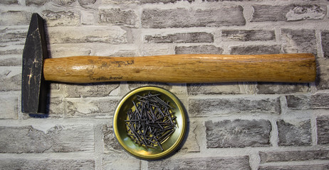 Black nails on a metal stand with a hammer on a brick wall background.