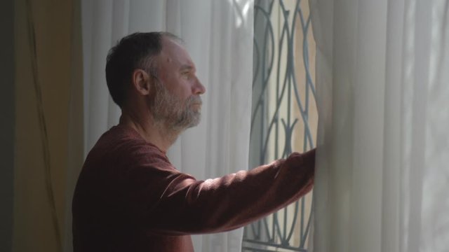Sad elderly man looks out the window.