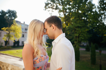 Lovely couple walking around the block. Dark-haired man in a white shirt hugging a blonde in a beautiful dress