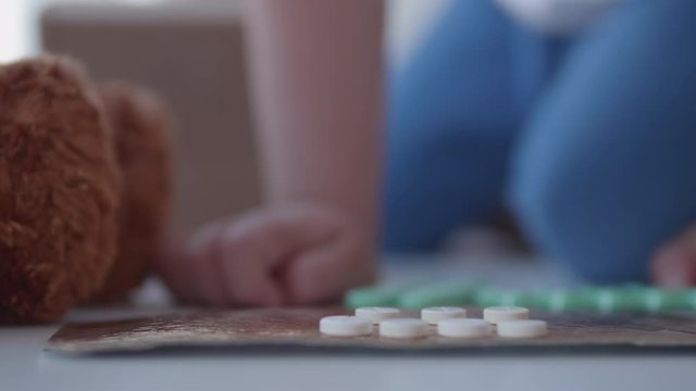 Kid plays with scattering medicine drugs. Toddler touches pills without parent control. Dangerous situation.