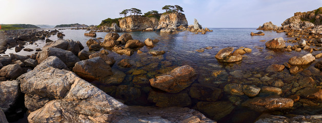 Rocky high island in the ocean. Rocky high island in Orlik Bay in the Sea of Japan. In the foreground are stones and clear water. Far East.
