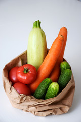 Fresh vegetables in paper packaging on white table and gray wall