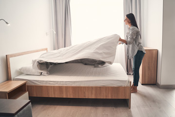 Charming young female person making her bed - obrazy, fototapety, plakaty