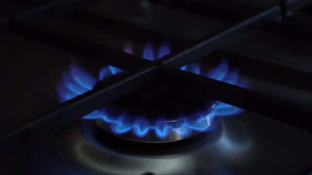 The kitchen burner turns on. The upper burner lights up, turning into a blue flame. Natural gas inflammation, close up.