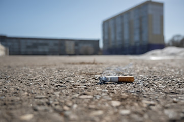 a Smoking abandoned cigarette butt lies on an asphalt pedestrian path on a city street