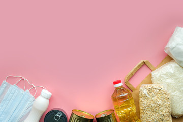 a set of necessary products during the quarantine period, cereals, sunflower oil, canned food, eggs, pasta, sugar, medical masks, free assistance, pink background. space for text