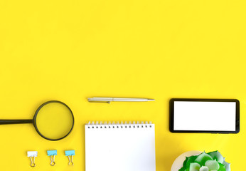 Minimalist office flat lay with mobile phone, magnifying glass, notebook and succulent on yellow background. Job searching or distance learning  concept. Banner with copyspace.