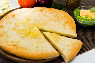 Ossetian pie with cheese on a wooden stand and a brown Mat, with ingredients. One piece was cut off.