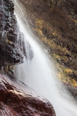 Obraz premium Stunning close up details of powerful waterfall cascading down the red, wet rocks and soft, background sunlit golden grass