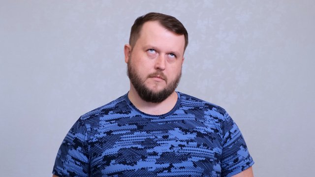 Tired fat bearded man in a blue T-shirt rolls his eyes. He was tired of work or tired of listening to his wifes conversation