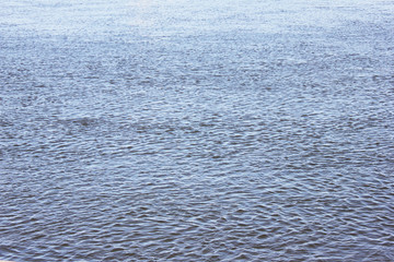 Light blue water surface background. Sea, pond, lake or river clear water with small wavy pattern, wind ripples on bright water surface. Nature concept image, blank coastal scenic landscape