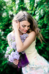 Beautiful girl in a summer dress with a bouquet of lilacs in a blooming garden. Romantic portrait outdoors