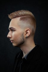 Portrait of handsome young guy against studio background. Perfect hairstyle, modern stylish haircut. Attractive guy with fashion hairstyle. Confident man with short beard. Barbershop concept.