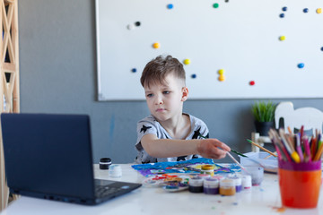 boy paints, online drawing classes, gray Tshirt with stars, laptop on the table