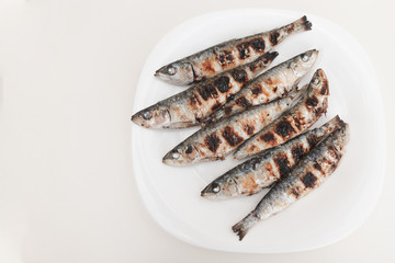 Freshly grilled sardines on a white plate. White background. Typical Mediterranean cuisine. Mediterranean gastronomy. Healthy food. Typical Spanish and Portuguese dishes.