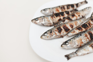 Freshly grilled sardines on a white plate. White background. Typical Mediterranean cuisine. Mediterranean gastronomy. Healthy food. Typical Spanish and Portuguese dishes.