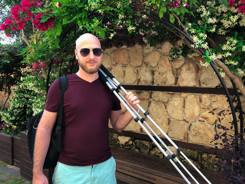 A young bearded male photographer with a tripod in his hand is walking in Antalya old town Kaleici. Horizontal image.