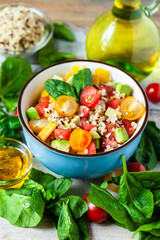 Concept of healthy food, clean eating, low calories delicious meal. Salad with quinoa and fresh vegetables with olive oil in blue bowl. Ripe tomato, avocado, spinach. Close up, wooden background