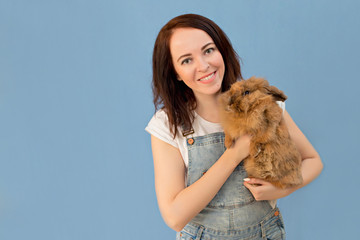 Portrait of a happy, cute girl 30-33 years old on an isolated blue background. A woman holds a rabbit in her hands.