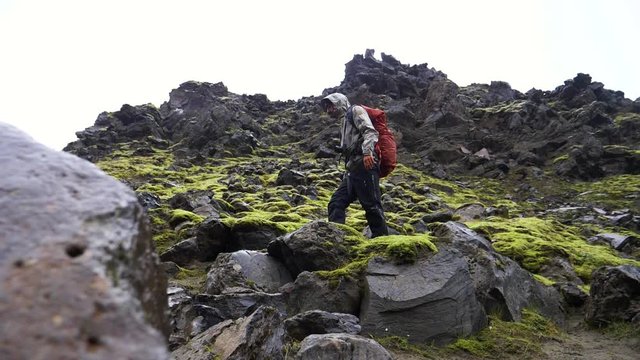 Hiker trekking in rocky and mossy nature, on a overcast, summer day, in Iceland - Low, slow motion shot