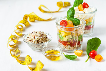 Concept of healthy food, clean eating, low calories delicious meal. Salad with quinoa and fresh vegetables with olive oil in glass jar. Tape measure, zero waste no plastic. Close up white background