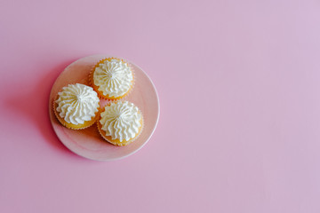 Vanilla cupcakes with cream cheese frosting and a cup of coffee on pink background. Sweet food concept. 