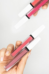 Vertical photo. Pink lip gloss in tube template. Lipstick color swatch set. Colored closed bottles of liquid lipstick and lip gloss arranged in a row on clean white or grey background. Space for text
