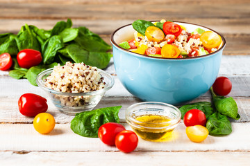 Concept of healthy food, clean eating, low calories delicious meal. Salad with quinoa and fresh vegetables with olive oil in blue bowl. Ripe tomato, avocado, spinach. Close up, wooden background