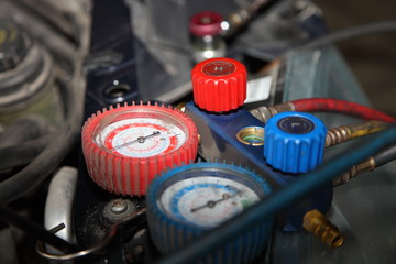 Car A/C red and blue manometers and valves close up under the hood of the car, automobile air conditioner repair pressure testing, service, vacuuming and refilling technology