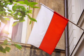 Polish white-red flag in wind on a high hill between silhouette of trees. Natural Light Selective Focus. building view. 1 of May, November 11, flag or independence or labor day. Government holiday