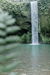 A branch in the foreground. Amazing waterfall Tibumana in Bangli, Indonesia, a stunning island. Jungle waterfall the best cascade in tropical rain forest with rock & turquoise blue pond.
