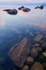 Fototapeta premium Lake Baikal in the summer at sunset. In the foreground is clear water and stones under water.
