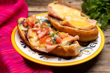 Mexican molletes with ham and cheese on wooden background