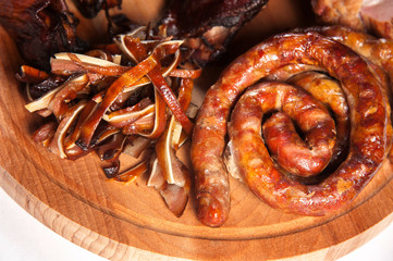 Home-fried natural sausage wrapped in a spiral. Near smoked meat on a wooden plate. Close-up.