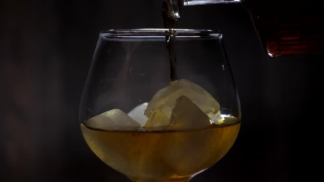 Pouring whiskey from the bottle into a glass with ice cubes