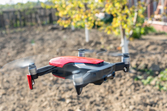 Small sized red drone with high resolution camera hovering in air for aerial photography.