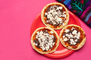 Mexican red sopes with cheese and beans on pink background