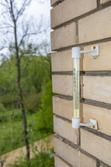 Outdoor vintage thermometer with numbers on a scale on a brick wall near a green park