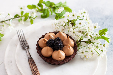 Chocolate tart with caramel filling and fresh blackberries. Cherry flowers on background. Copy space