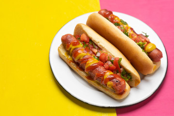 Hot dog with pico de gallo salad on pink and yellow background