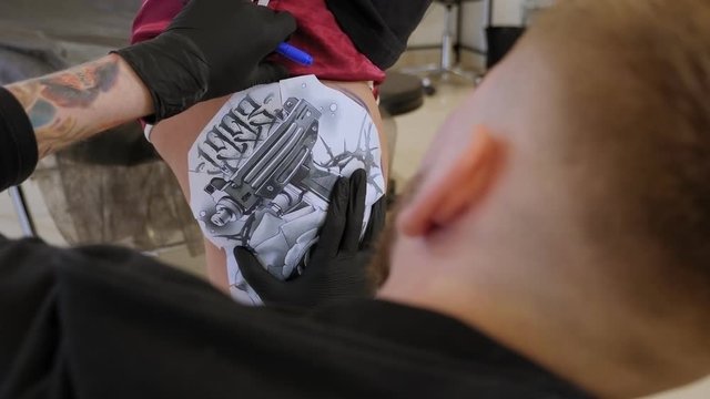 Tattoo artist puts a picture on the leg of a girl, the process of creating a tattoo. Tattooist doing picture on leg of woman. Close-up.