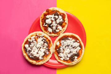 Mexican red sopes with cheese and beans on yellow and pink background