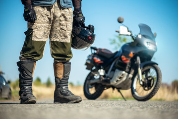 Biker with a helmet in hands is standing on the road close up.